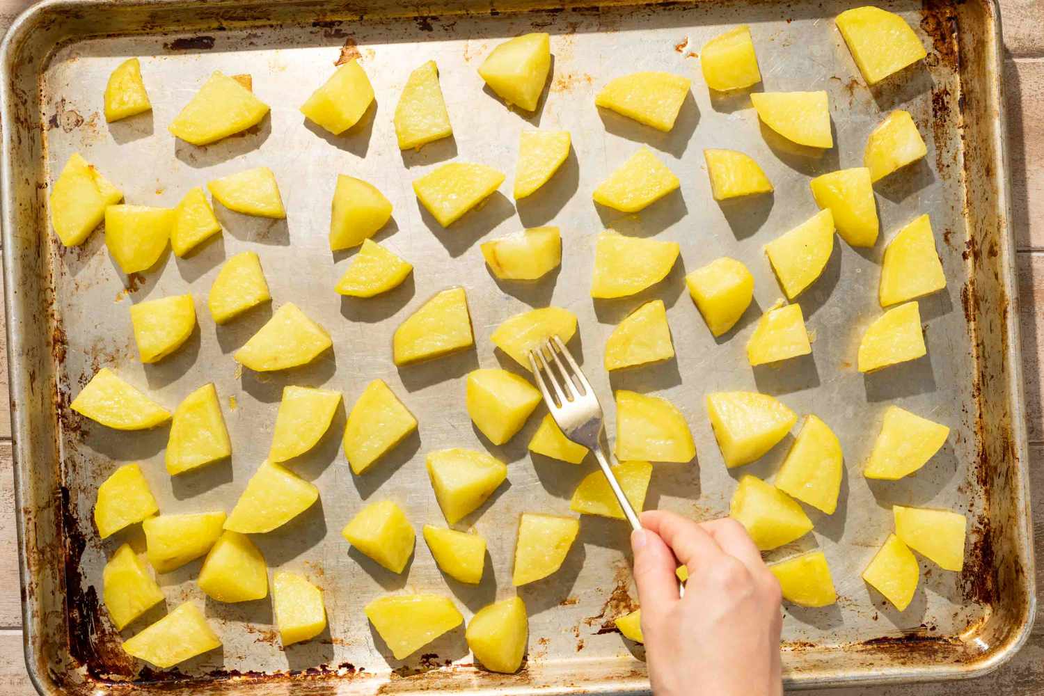 Overhead view of a hand flipping potato slices while roasting for Gamja Jorim (Korean Braised Potatoes) recipe