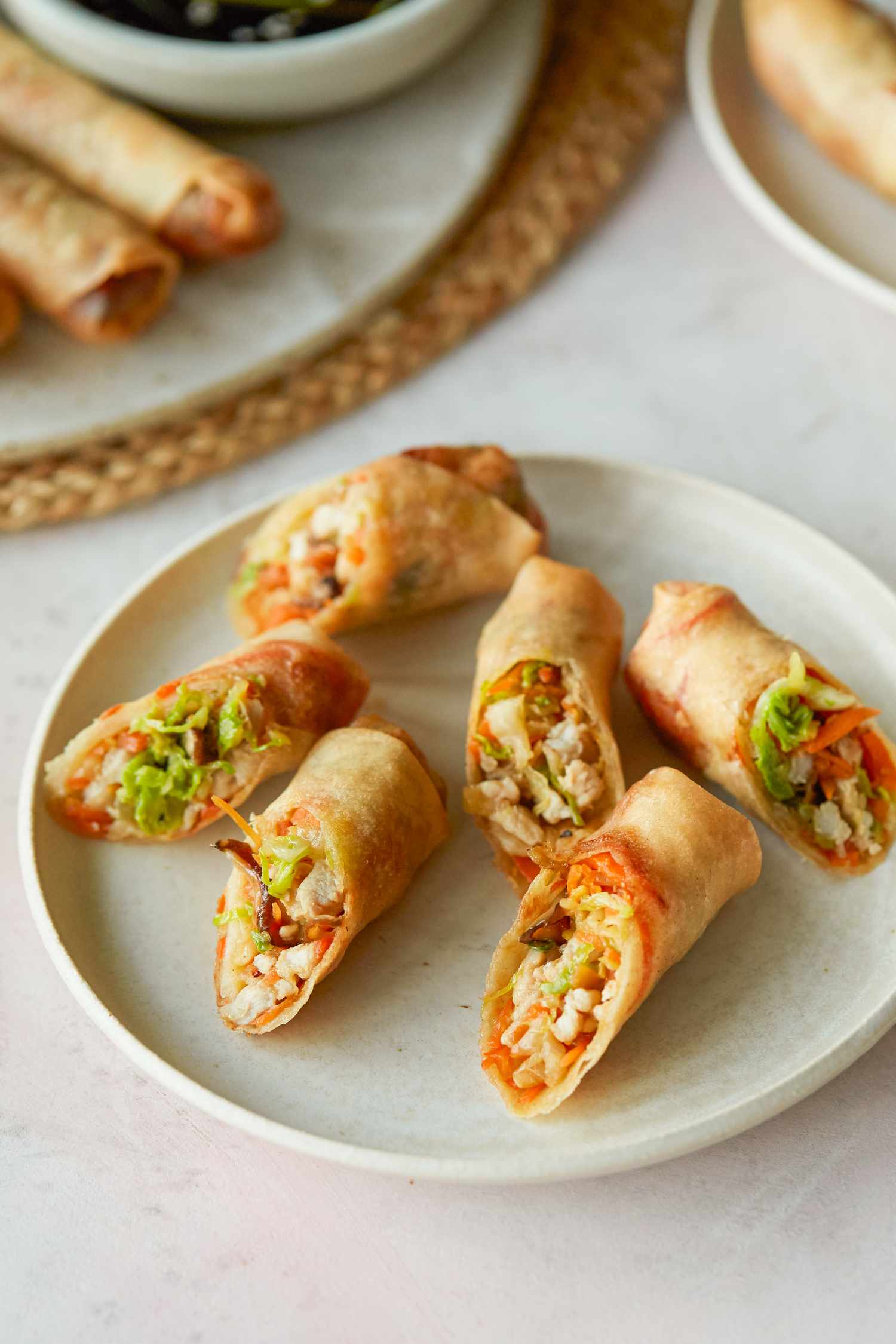 A plate of fried spring rolls cut in half and with whole spring rolls behind it on a platter.