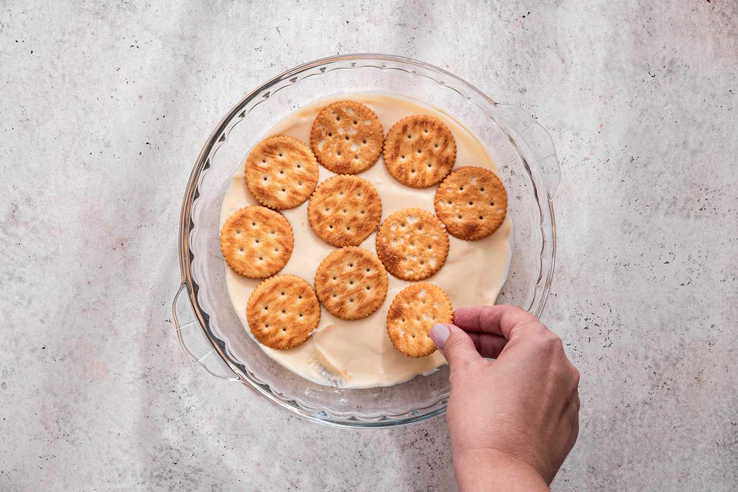 A layer of Ritz crackers being added to the pie plate for lime icebox cake