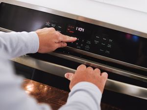 Hands adjusting the controls on an oven to preheat