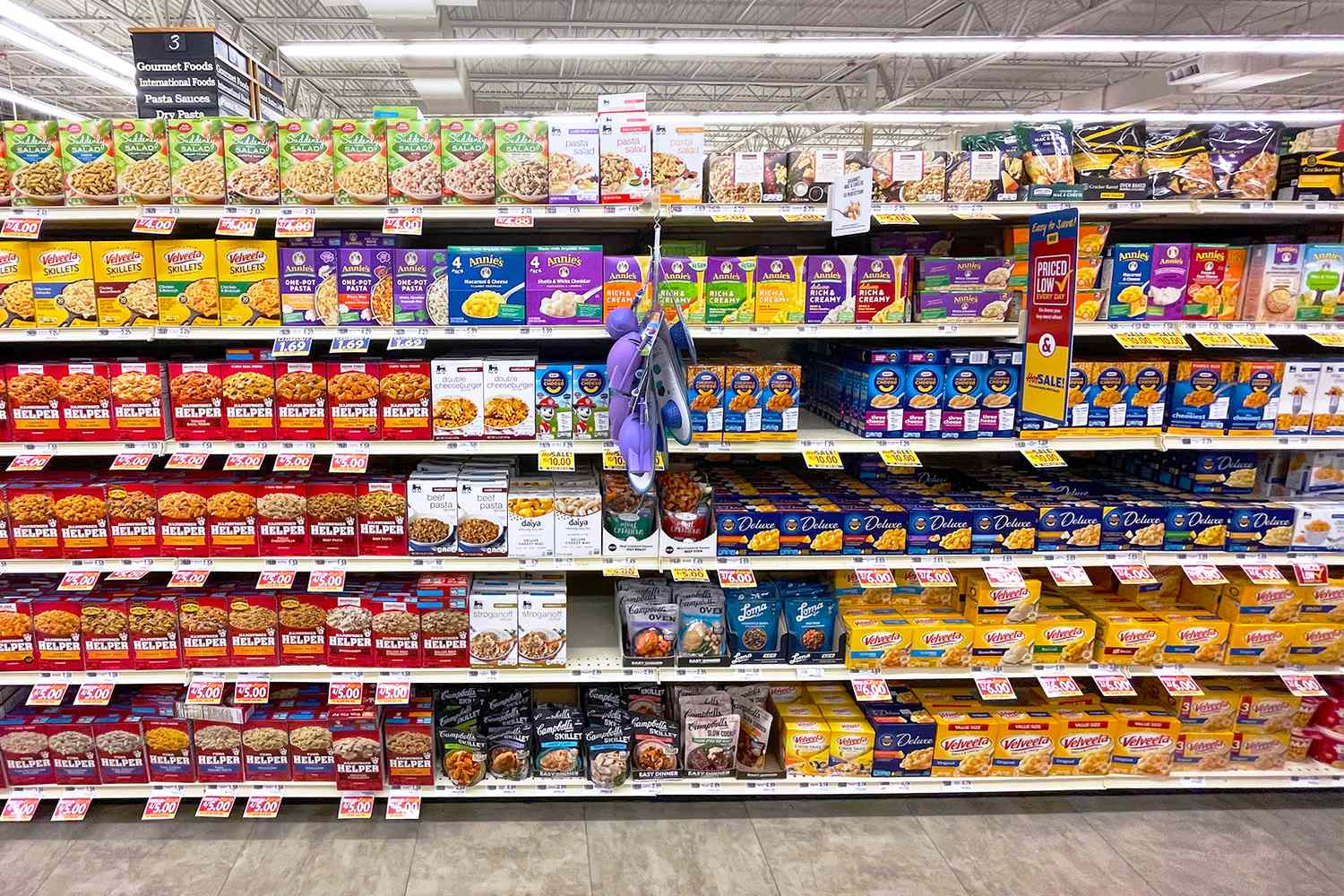 Shelves stocked with various brands of boxed macaroni and cheese in a grocery store aisle