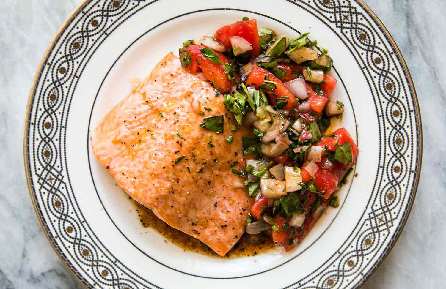 Salmon Provencal with tomatoes on a white plate with a design on the rim