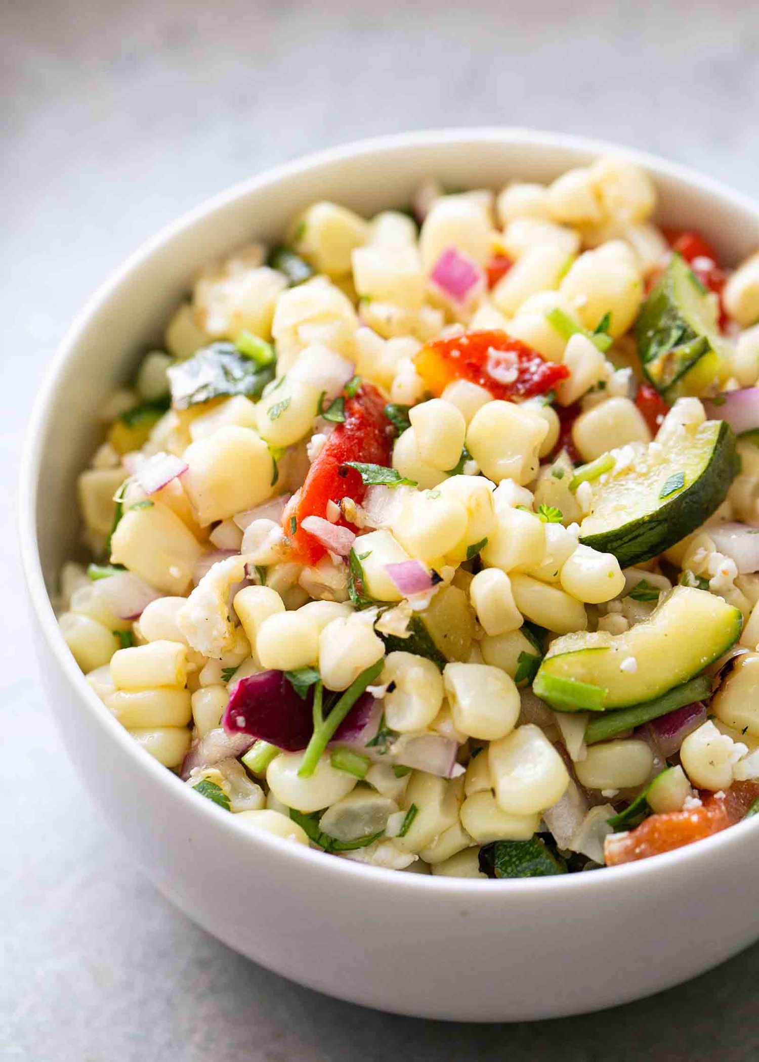 A bowl of mixed grilled corn salad with chopped vegetables like red onion, bell pepper, and zucchini