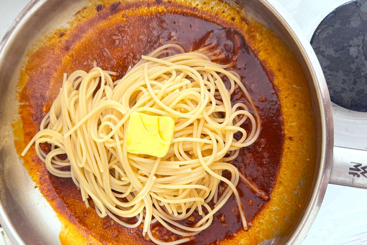 Spaghetti in a pan with spicy sauce and a piece of butter on top