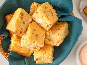 A basket of sliced cornbread on a blue cloth accompanied by a dish of sauce