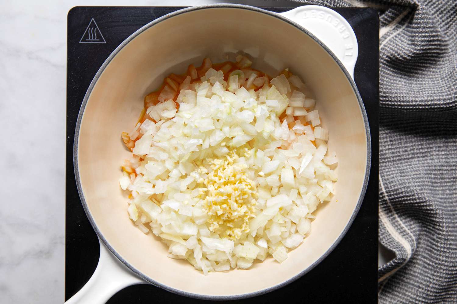 Onions, Garlic, and Annatto Oil in a Dutch Oven on a Portable Burner Next to a Gray Kitchen Towel for Banana Ketchup Recipe