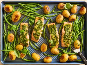 A sheetpan with salmon fillets topped with pesto, green beans, potatoes and basil