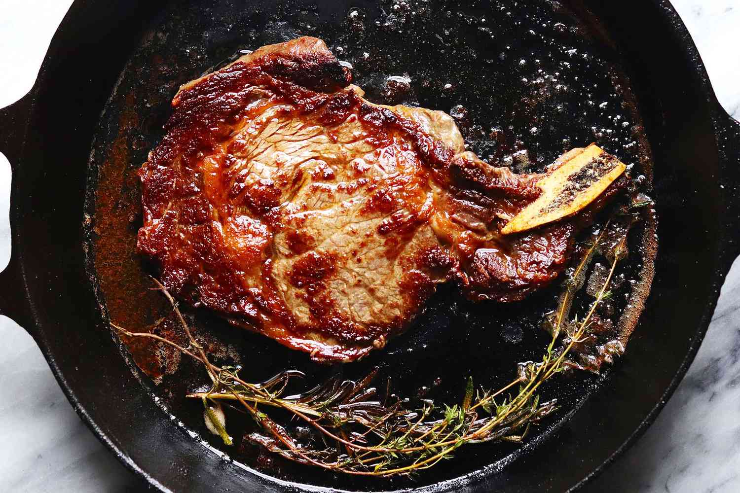 A cooked steak with herbs in a cast iron skillet