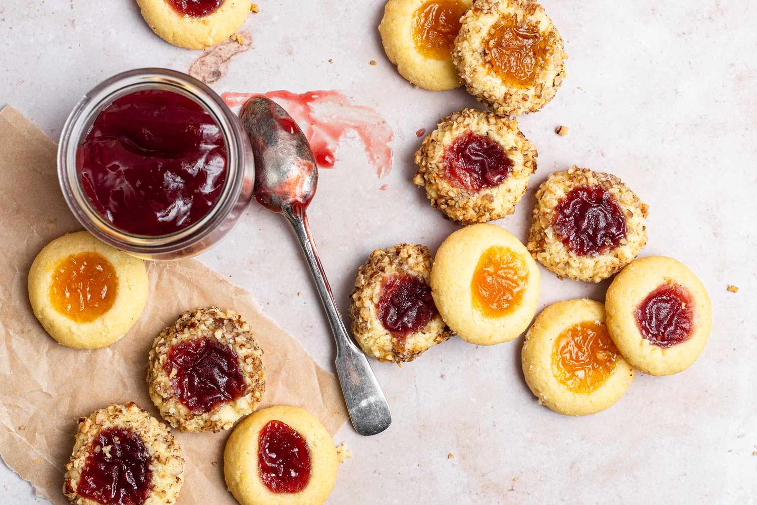 Classic thumbprint cookies spread on parchment paper and a spoonful of jam next to them.