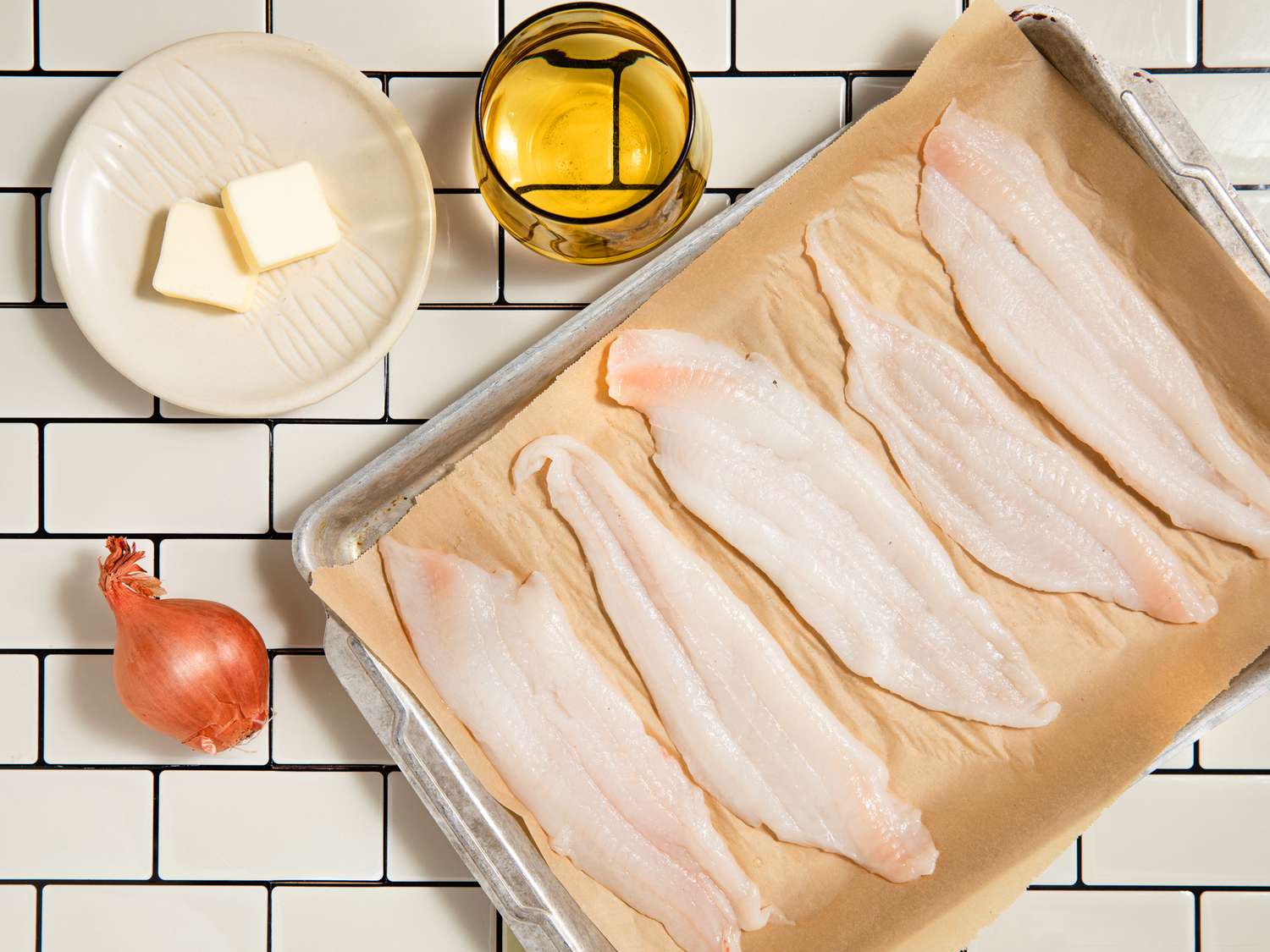 Raw fish fillets on a baking sheet with butter, onion, and wine on the side