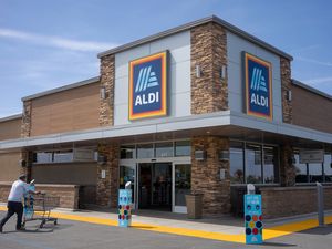 An Aldi grocery store exterior and a shopper pushing a cart in the parking lot