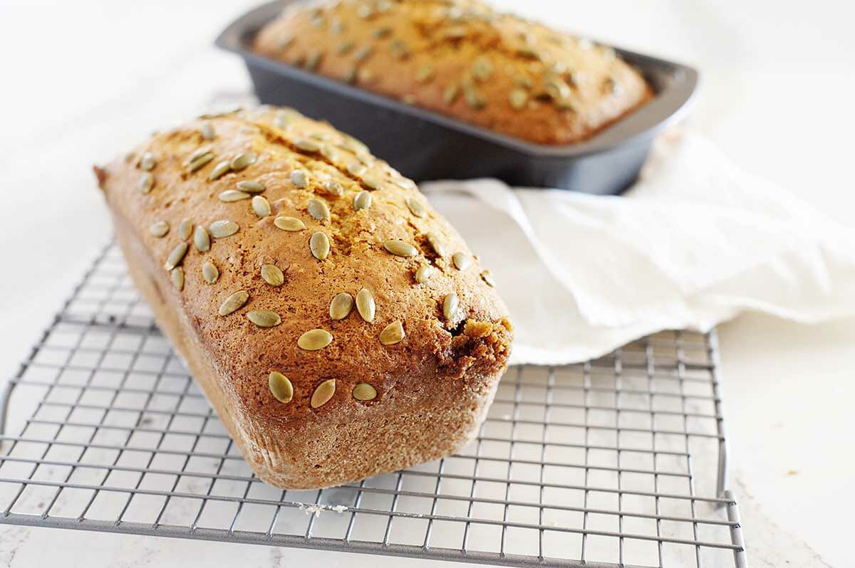 A loaf of moist Pumpkin Bread cooling on a rack with a second loaf in a pan behind it.