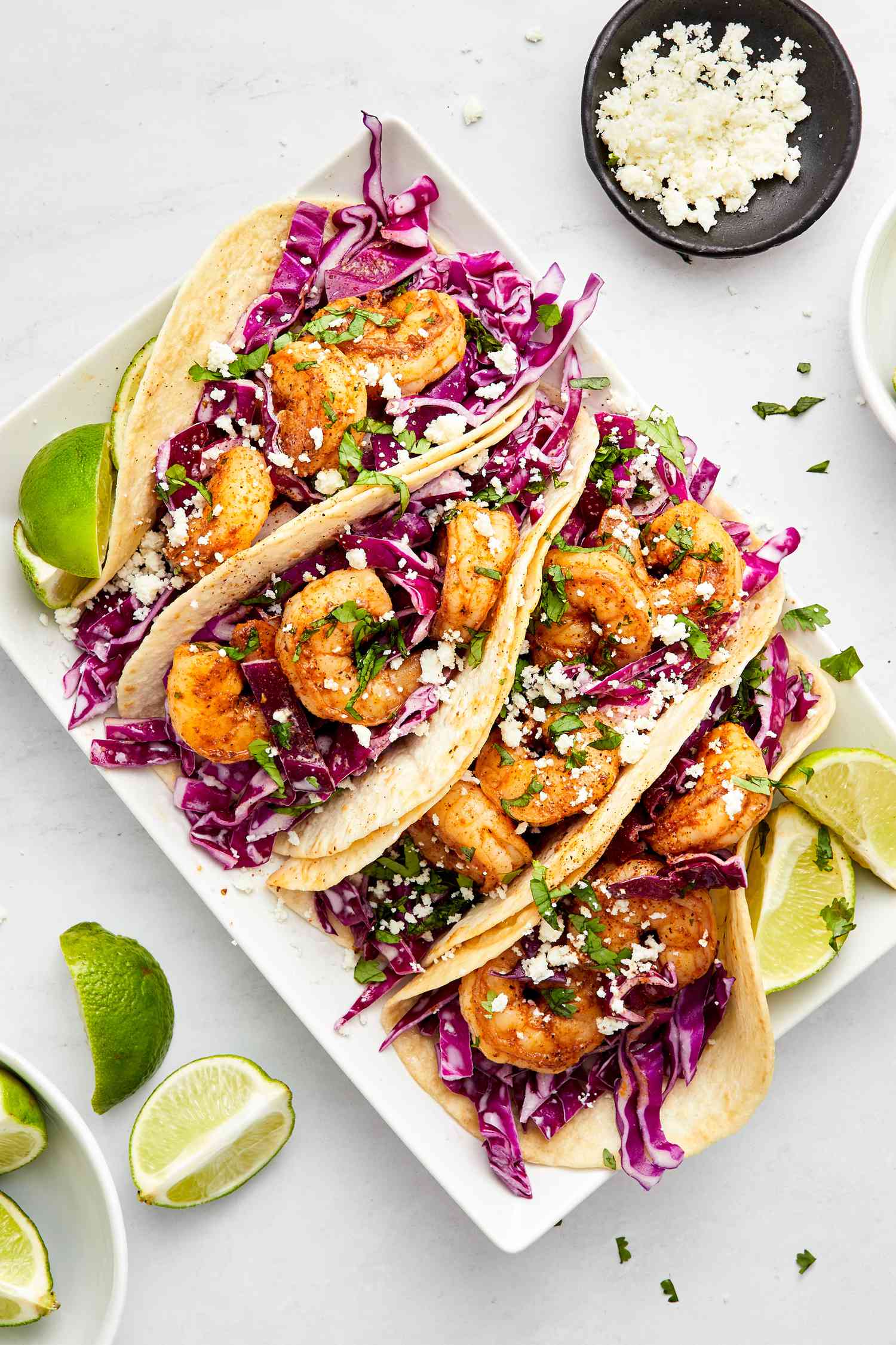 Blackened Shrimp Tacos and Lime Wedges on a Plate Surrounded a Bowl of More Lime Wedge and a Bowl of Queso Fresco