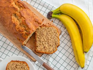 Banana bread loaf with a slice cut laying on the cutting board next to some bananas