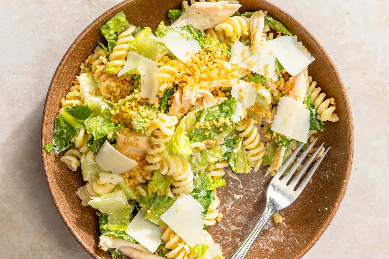 A bowl of pasta salad with chicken and shredded cheese on top, fork on the side