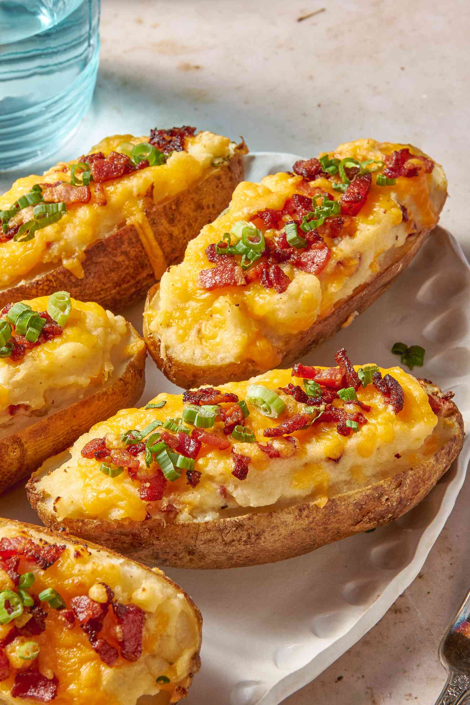 Twice baked potatoes on a platter next to a glass of water