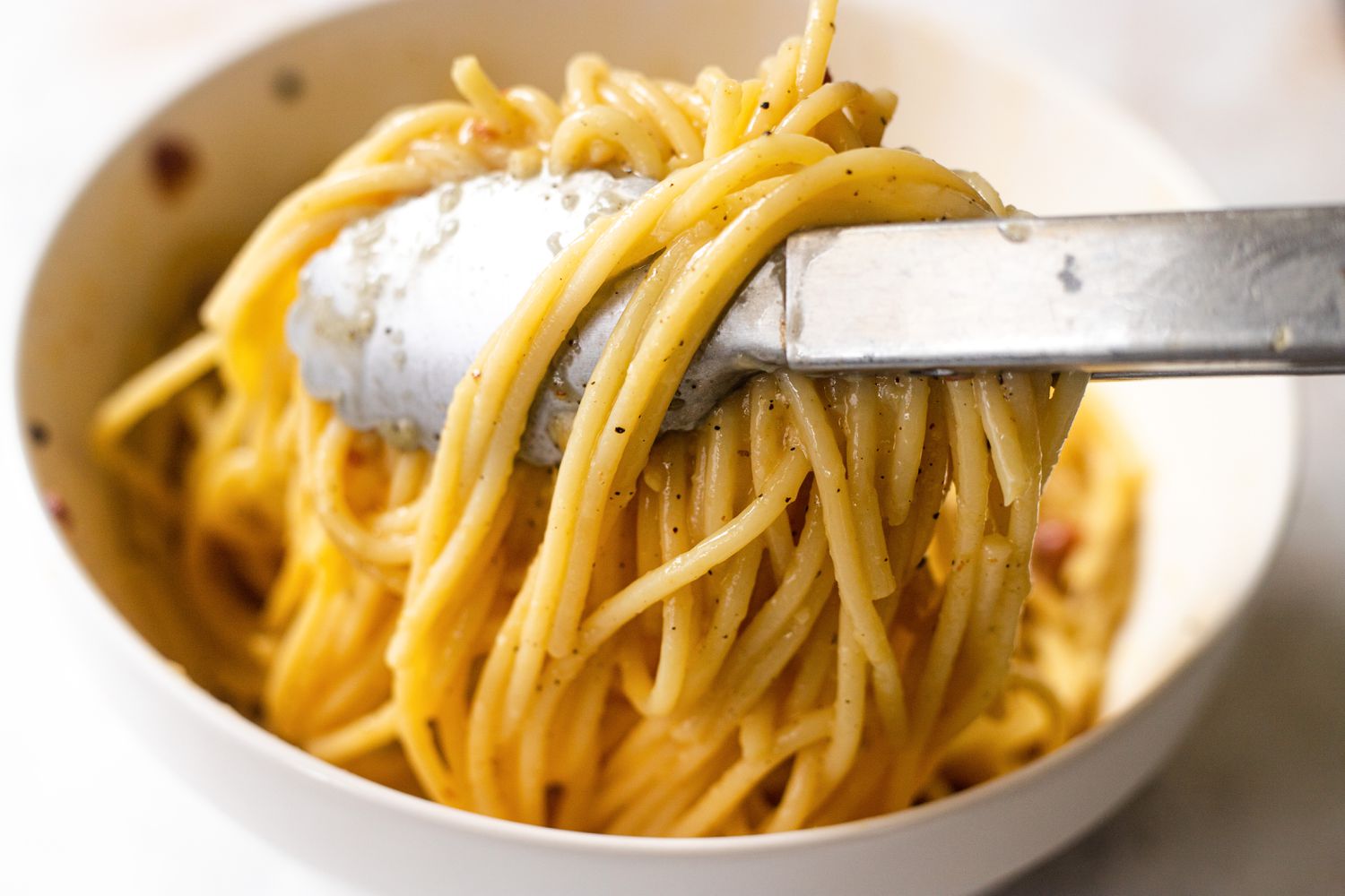 Tongs mixing pasta for Spaghetti Carbonara.