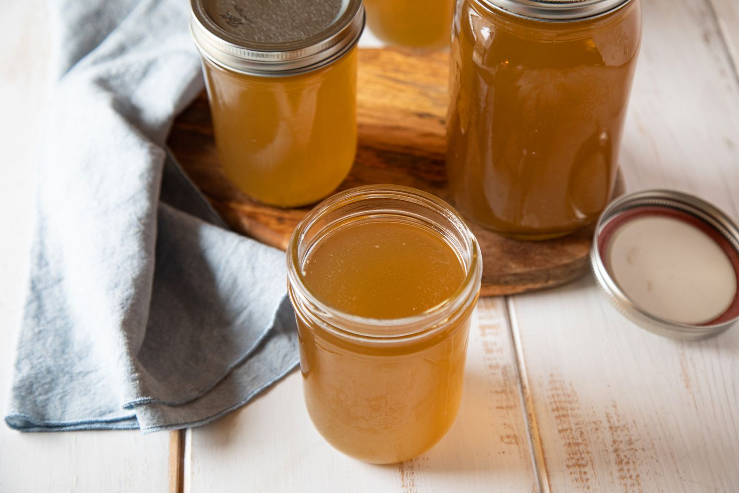 Mason jars of beef broth with the lid off the one in front.