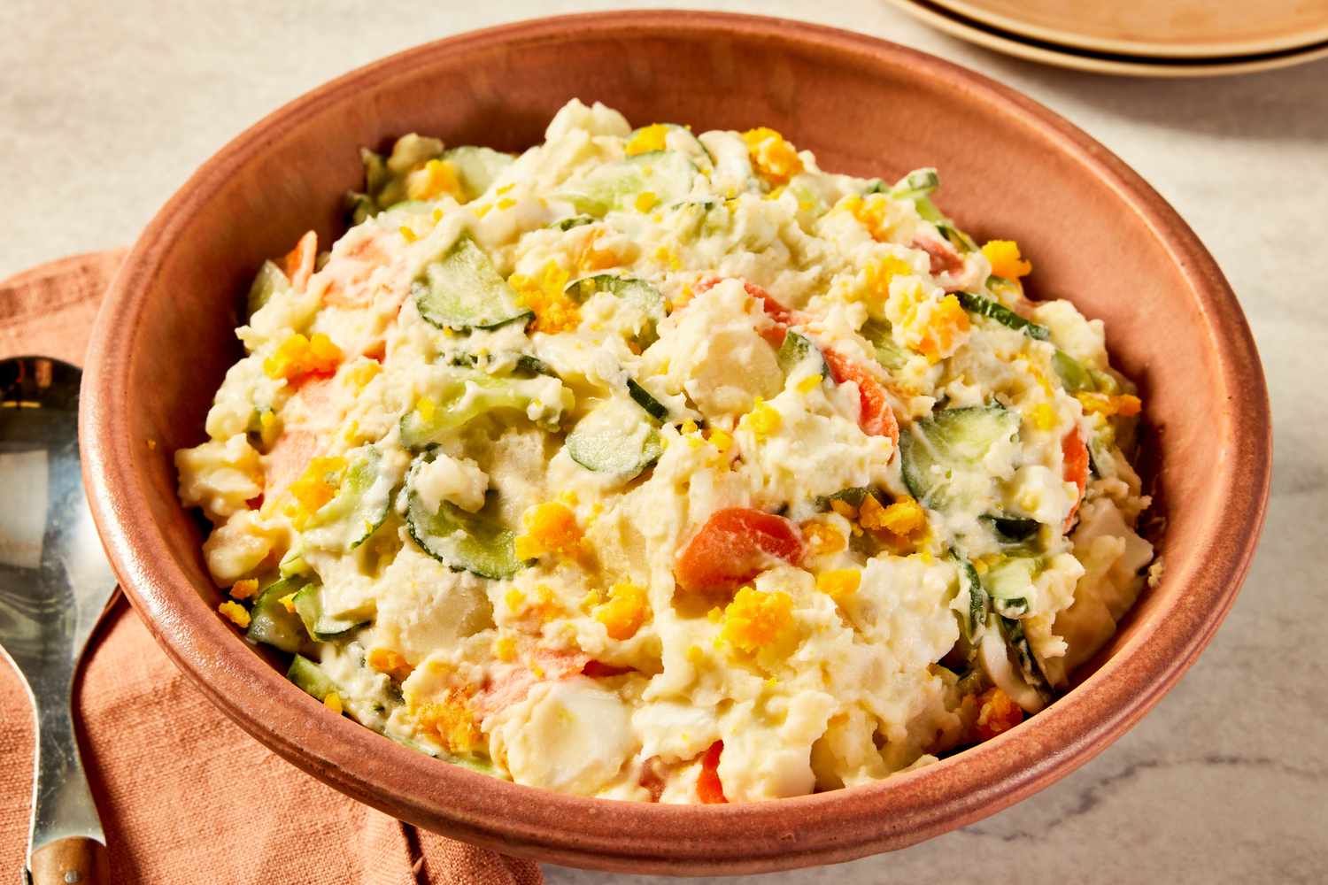 Korean-style potato salad in a bowl at a table setting with a stack of plates and a spoon