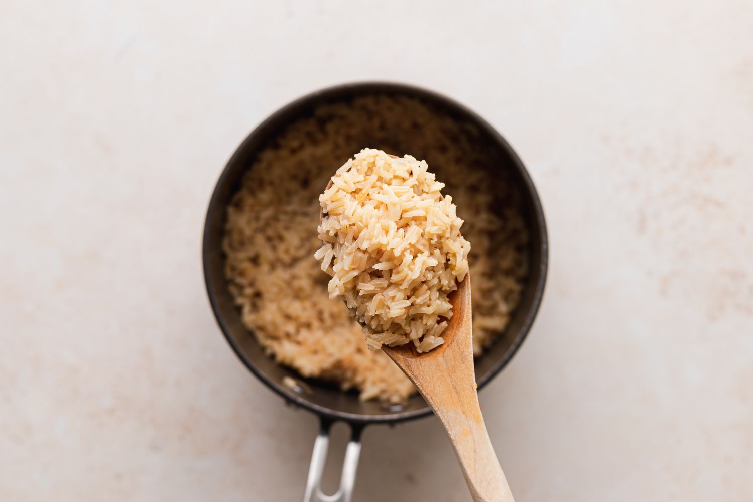 A wooden spoon scooping up cooked rice out of a pot.
