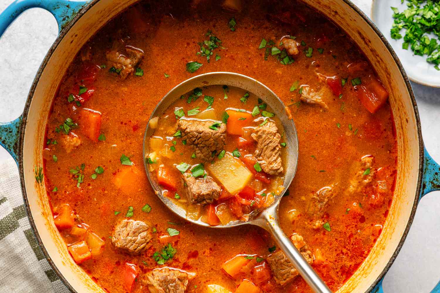 Overhead view of a dutch oven of Hungarian goulash with a ladle in the center with a serving inside