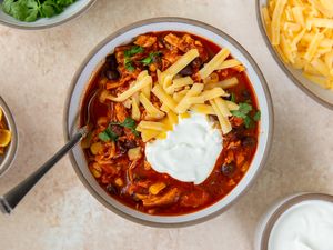 A bowl of chicken enchilada chili topped with shredded cheese sour cream and cilantro