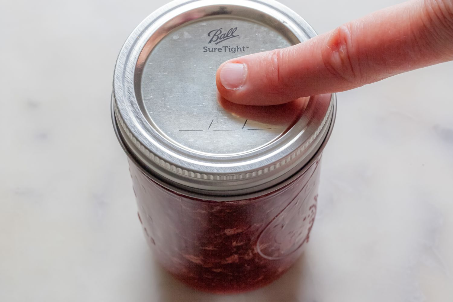 Pressing Jar of Strawberry Jam to Check for Popping Sound After Water Bath Canning Method