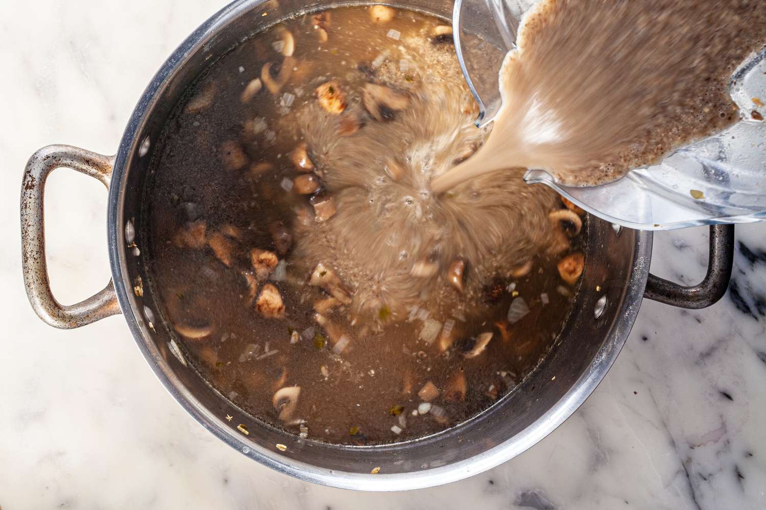 Adding blended cremini mushroom and chestnut soup to the stockpot.