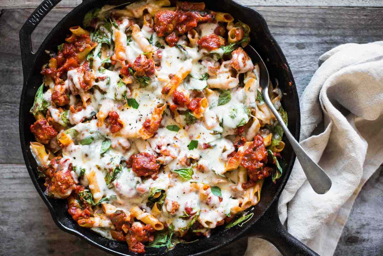 A cast iron skillet with chicken sausage, pasta, and melted cheese