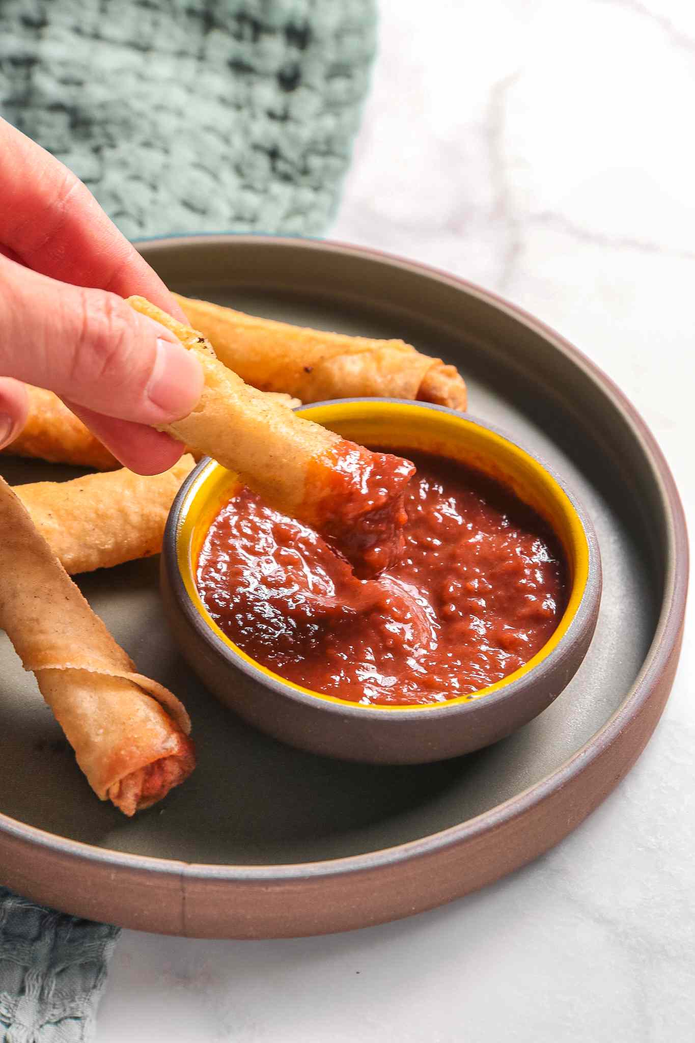 Lumpia Dipped in a Bowl of Banana Ketchup. Bowl Sitting on a Plate With More Lumpia
