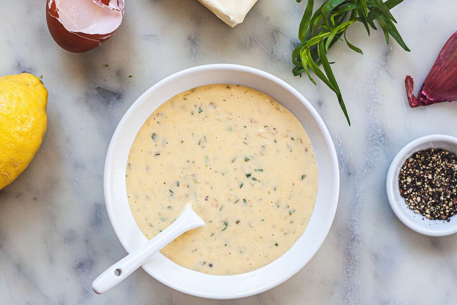 Overhead view of Béarnaise sauce with shallots, herbs, and lemon around the bowl.