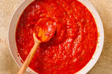 A wooden spoon in a bowl of tomato sauce evenly spread and textured