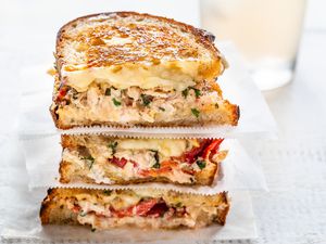 Grilled tuna sandwich cut in half and stacked on top of each other. The bread is toasted and tuna, melted cheese and tomatoes are visible in the filling.