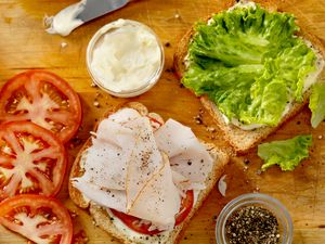 Preparation of a sandwich with lettuce sliced tomatoes turkey and black pepper