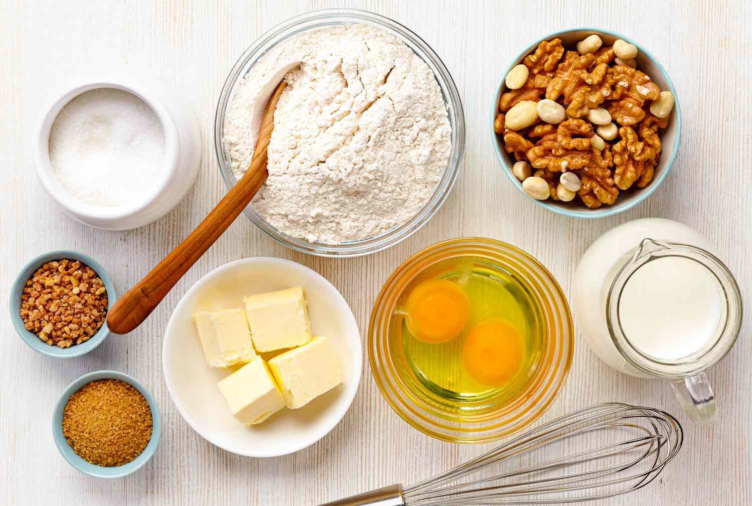 Baking ingredients: flour, eggs, sugar, butter, milk, nuts and spices on a white wooden background