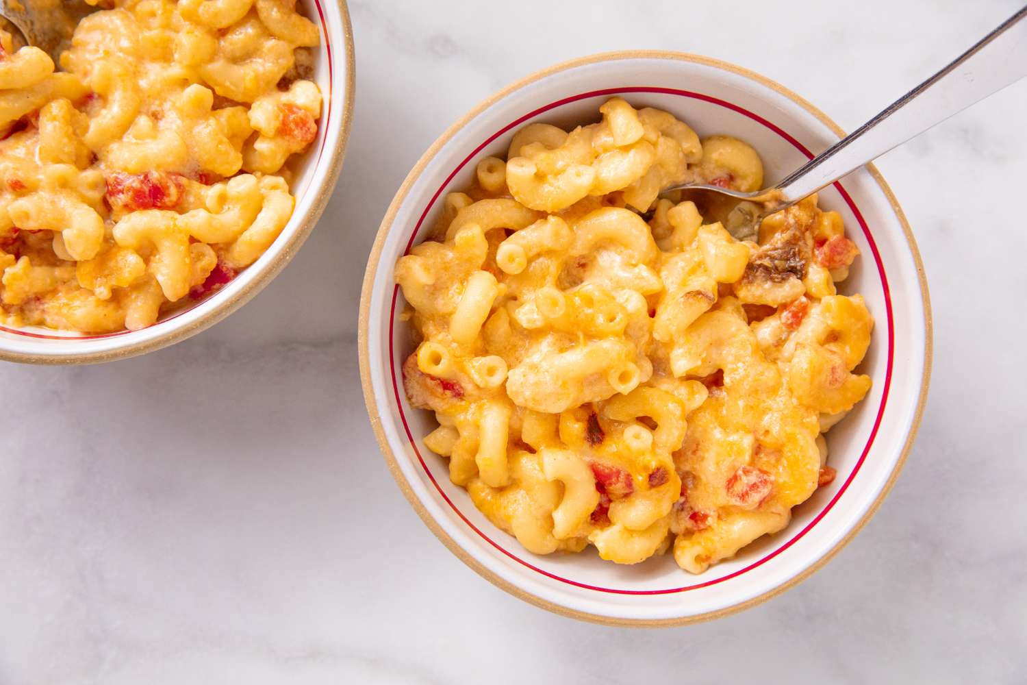 Bowls of macaroni and cheese on a table with one bowl showing a spoon inserted