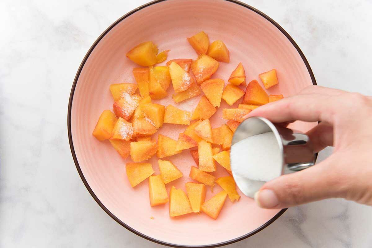 Chopped peaches being sprinkled with sugar to make homemade peach cobbler ice cream.