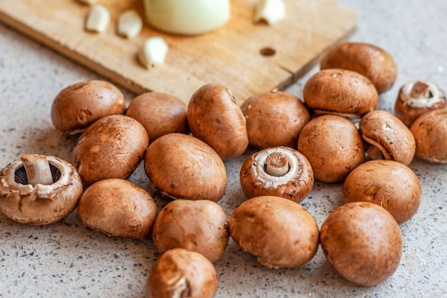 Closeup view of multiple mushrooms on a countertop with a wooden cutting board and garlic in the background