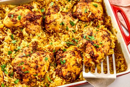 Baked chicken thighs on seasoned rice in a rectangular baking dish with a serving spatula