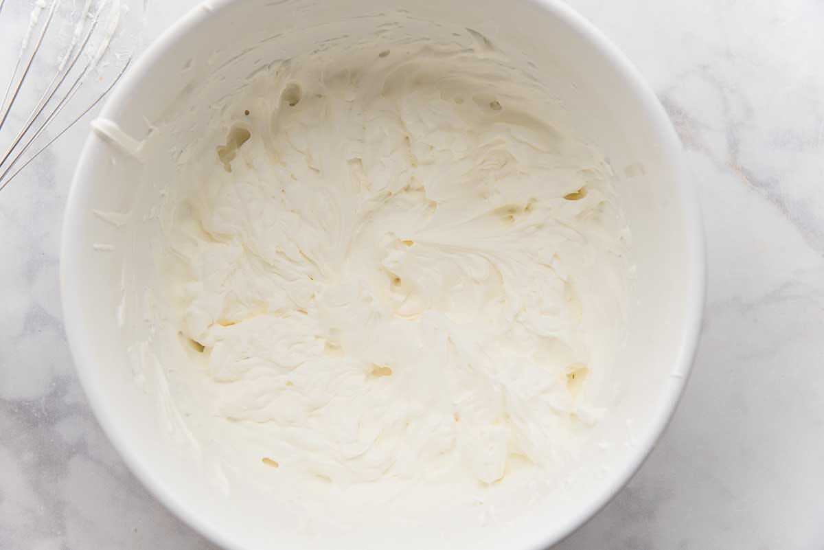 A white bowl with whipped cream inside to make peach cobbler ice cream.