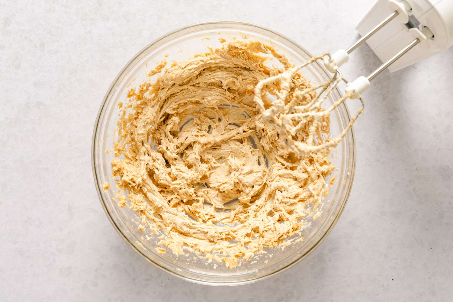 A mixing bowl with creamed batter next to a hand mixer