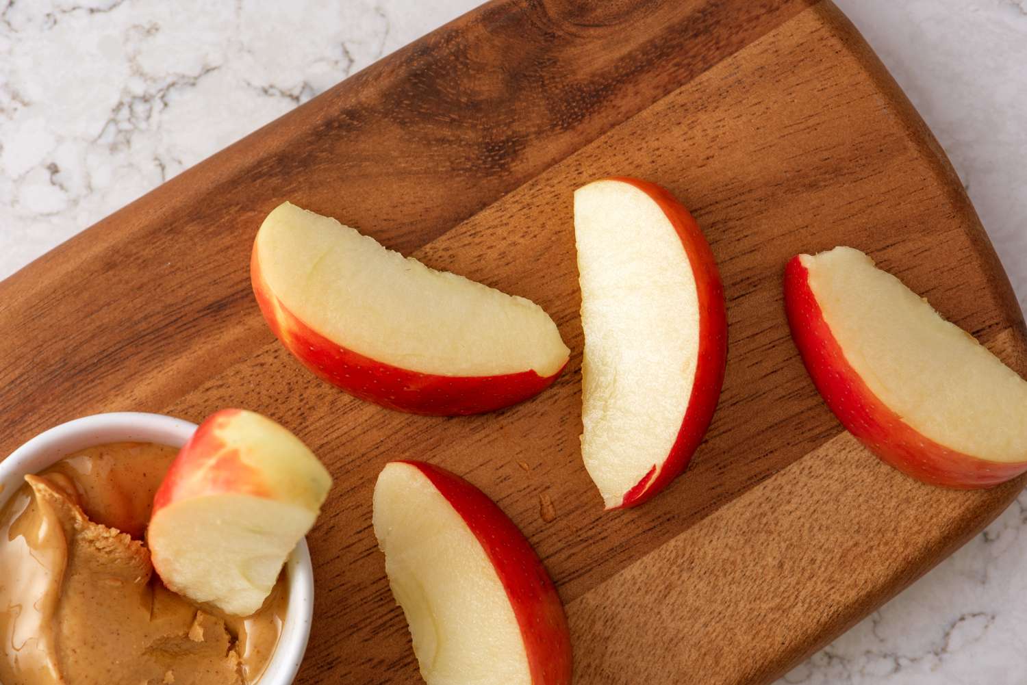 Apple slices on a wooden board next to a bowl of peanut butter