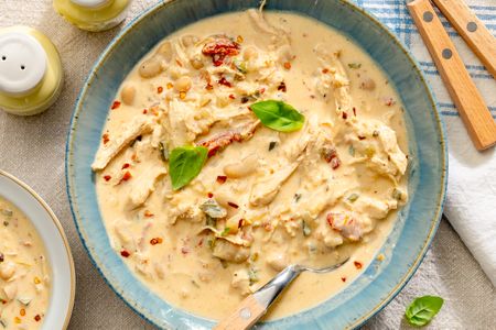 A bowl of creamy Marry Me Chicken Chili garnished with herbs and spices with a spoon resting inside