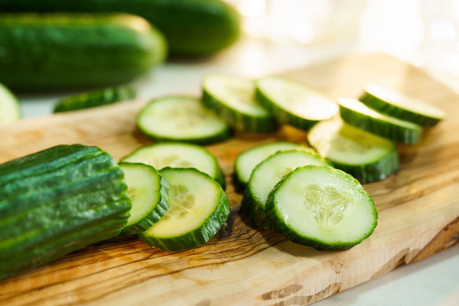 Sliced cucumbers on a wooden cutting board, with a whole cucumber in the background