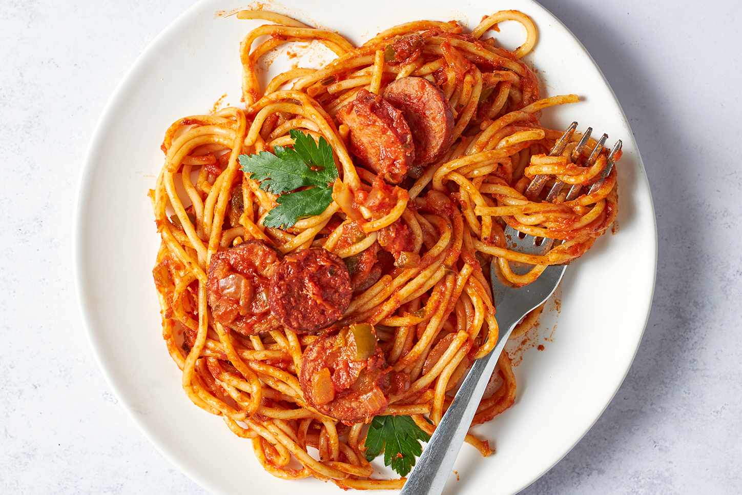 A plate of creole spaghetti with sausage and herbs garnished on a white background
