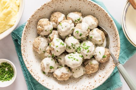 A bowl of meatballs covered in a creamy sauce garnished with parsley