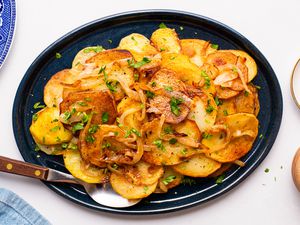 Lyonnaise potatoes on a platter at a tablet setting with a small plate of crushed peppers, bowl of minced parsley, and a plate 