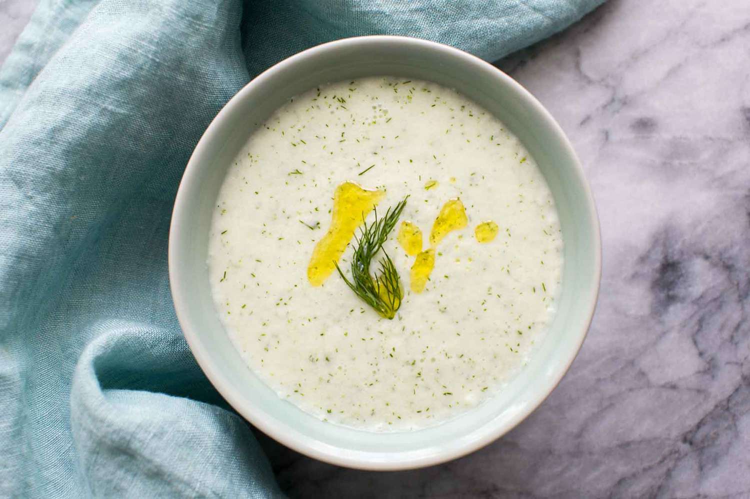 Cucumber Soup with a sprig of dill in a white bowl with a blue napkin