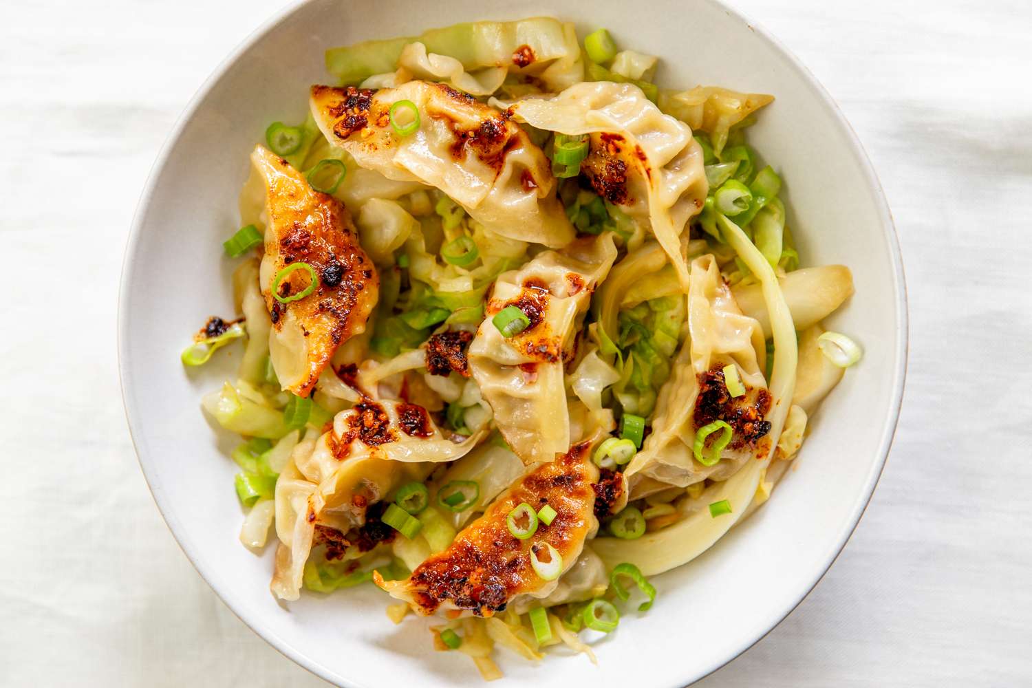 A bowl of gyoza dumplings over cabbage and garnished with green onions and chili sauces