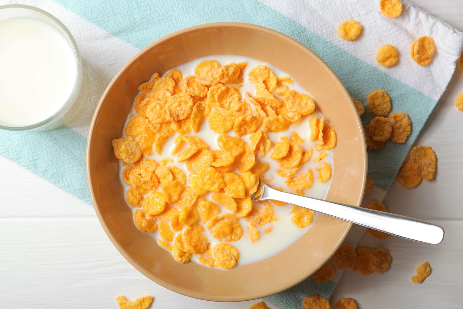 overhead view of a bowl of corn flakes with milk, a glass of milk on the side
